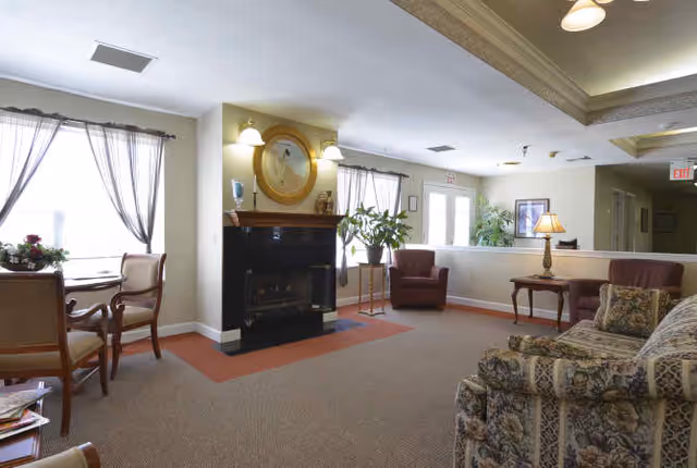 Cozy communal living room with sofas, armchairs, a fireplace, and a small table by curtained windows.