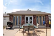 Patio in front of a single-story brick building featuring a table with chairs, a grill, and sliding glass doors under a clear sky.