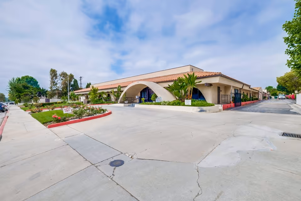 Exterior view of Arcadia Healthcare Center showing a single-story building with a curved arch entrance, surrounded by landscaped greenery and a driveway with an 'Enter Only' sign under a partly cloudy sky.