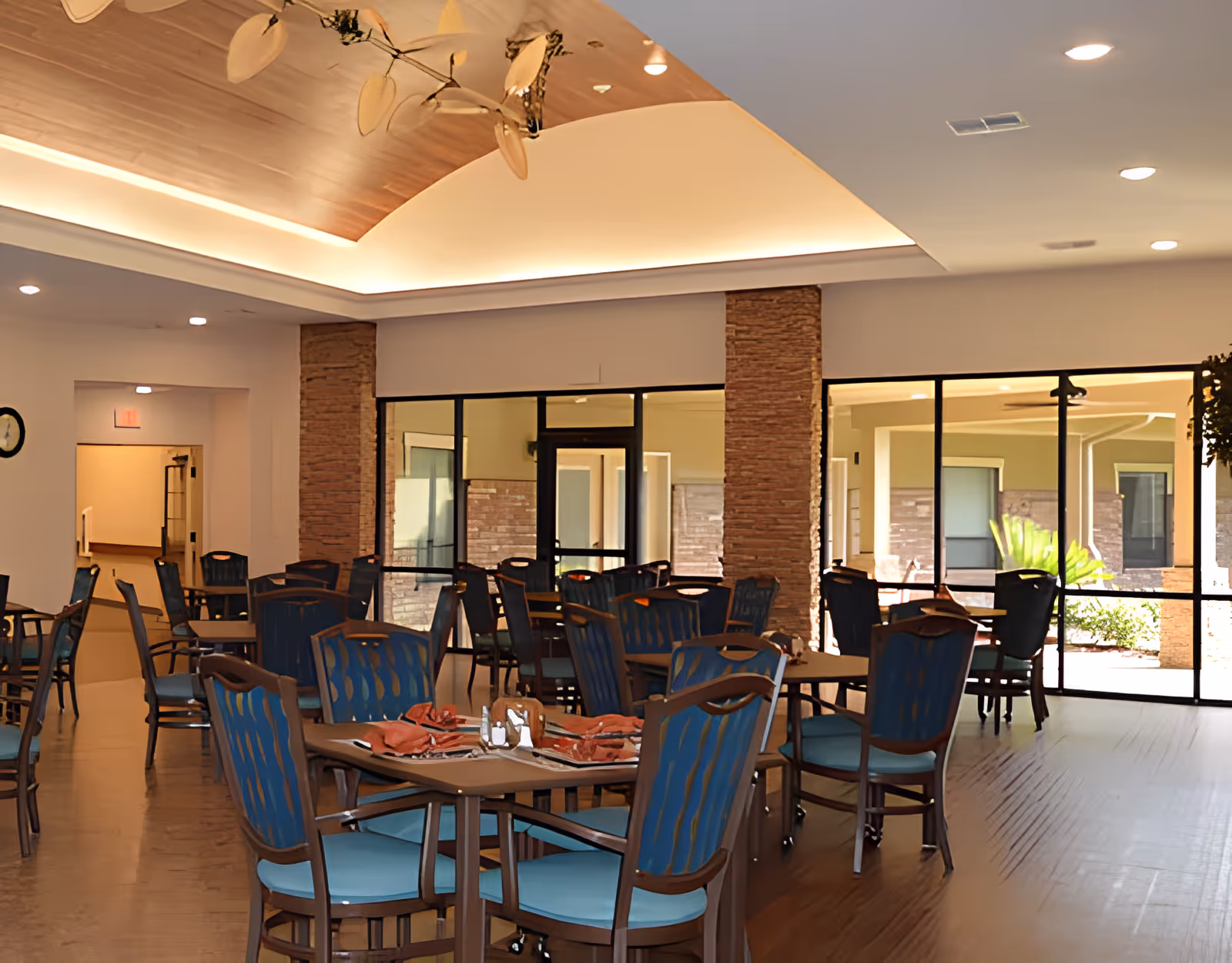 Bright dining room with multiple set tables and blue-upholstered chairs and large windows overlooking a courtyard.