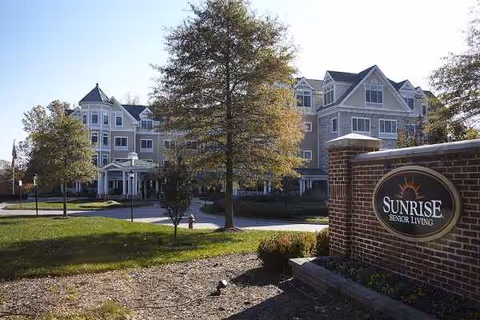 Exterior view of Sunrise Senior Living with brick sign and landscaped entrance.