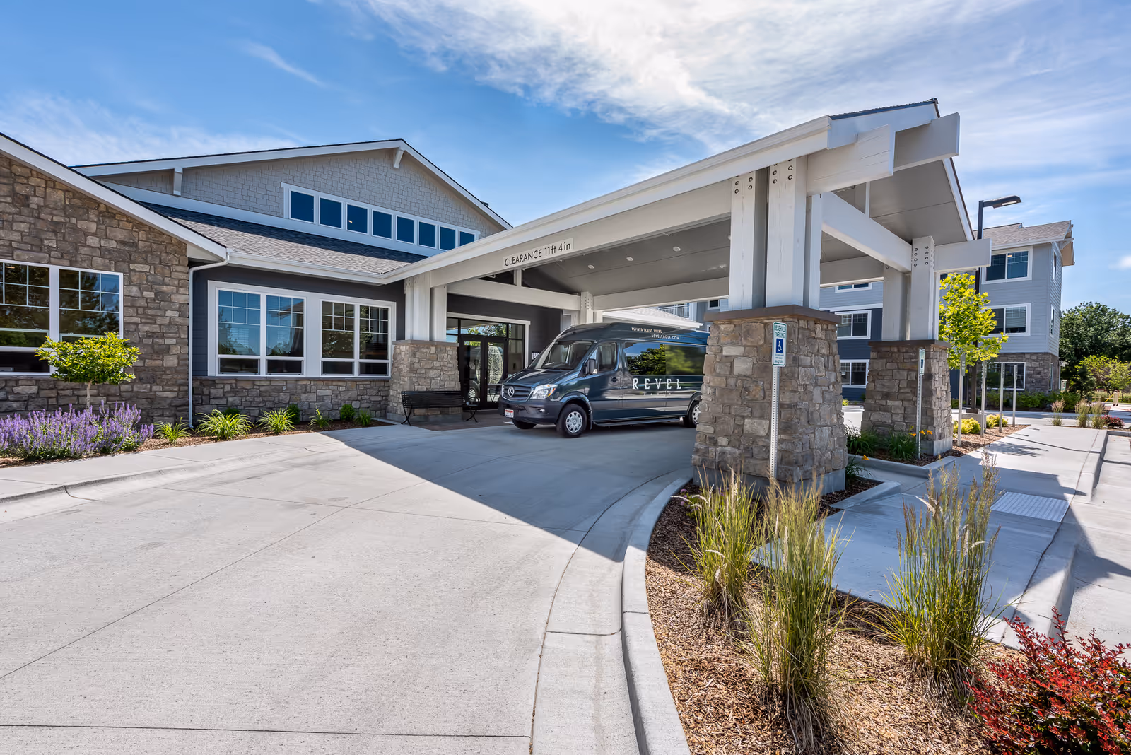 Exterior view of Revel Eagle senior living entrance with a covered drop-off and landscaped approach.