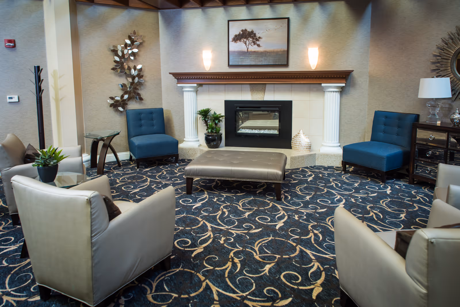 A comfortable lounge with armchairs, blue accent chairs, an ottoman, patterned carpet and a fireplace.