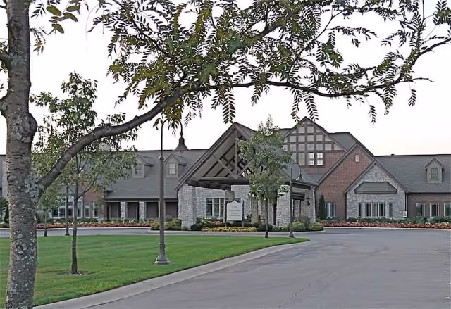 Exterior view of University Place Health Center And Assisted Living building with a driveway, green lawn, trees, and a covered entrance.