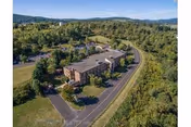 Aerial view of a multi-story brick nursing and rehabilitation center with a driveway and parking area, set among trees and rolling hills.