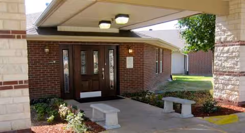 Exterior view of the facility entrance with brick facade, glass doors, and benches.