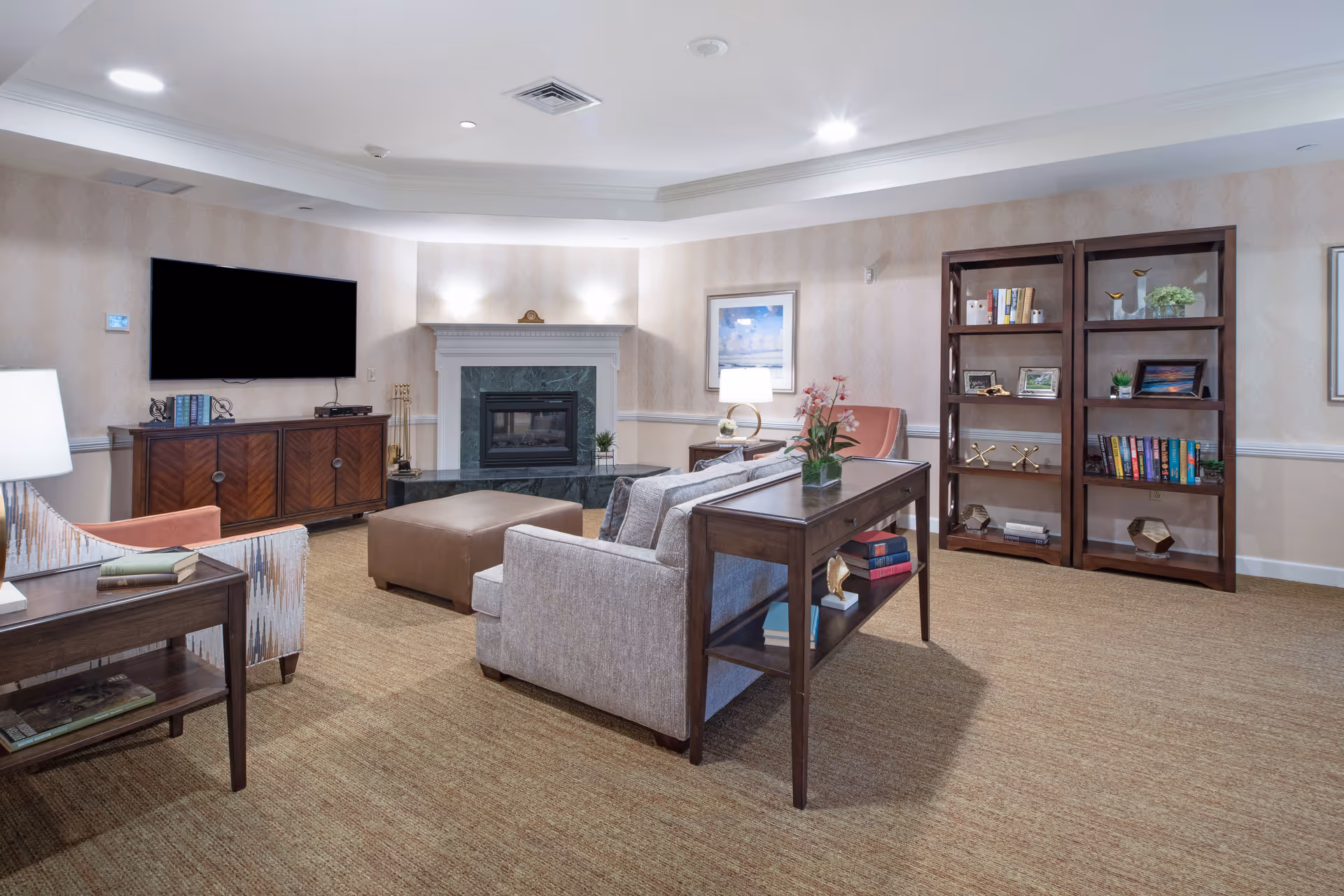 A comfortable common room with sofas, armchairs, bookshelves, a fireplace, and a wall-mounted TV.