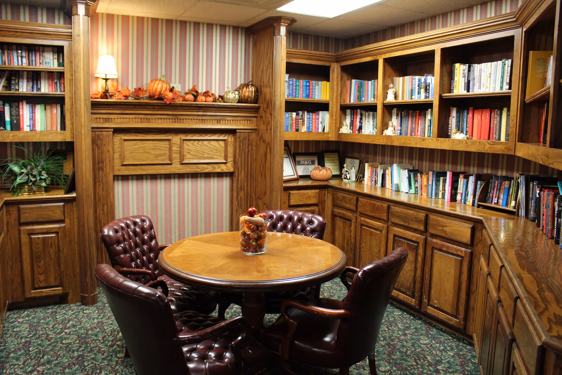 Cozy wood-paneled reading room with built-in bookshelves, a round table and four leather chairs.