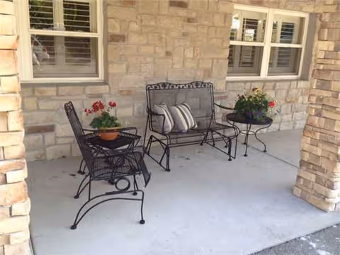 Stone-walled porch with wrought-iron chairs, cushions, and potted flowers.