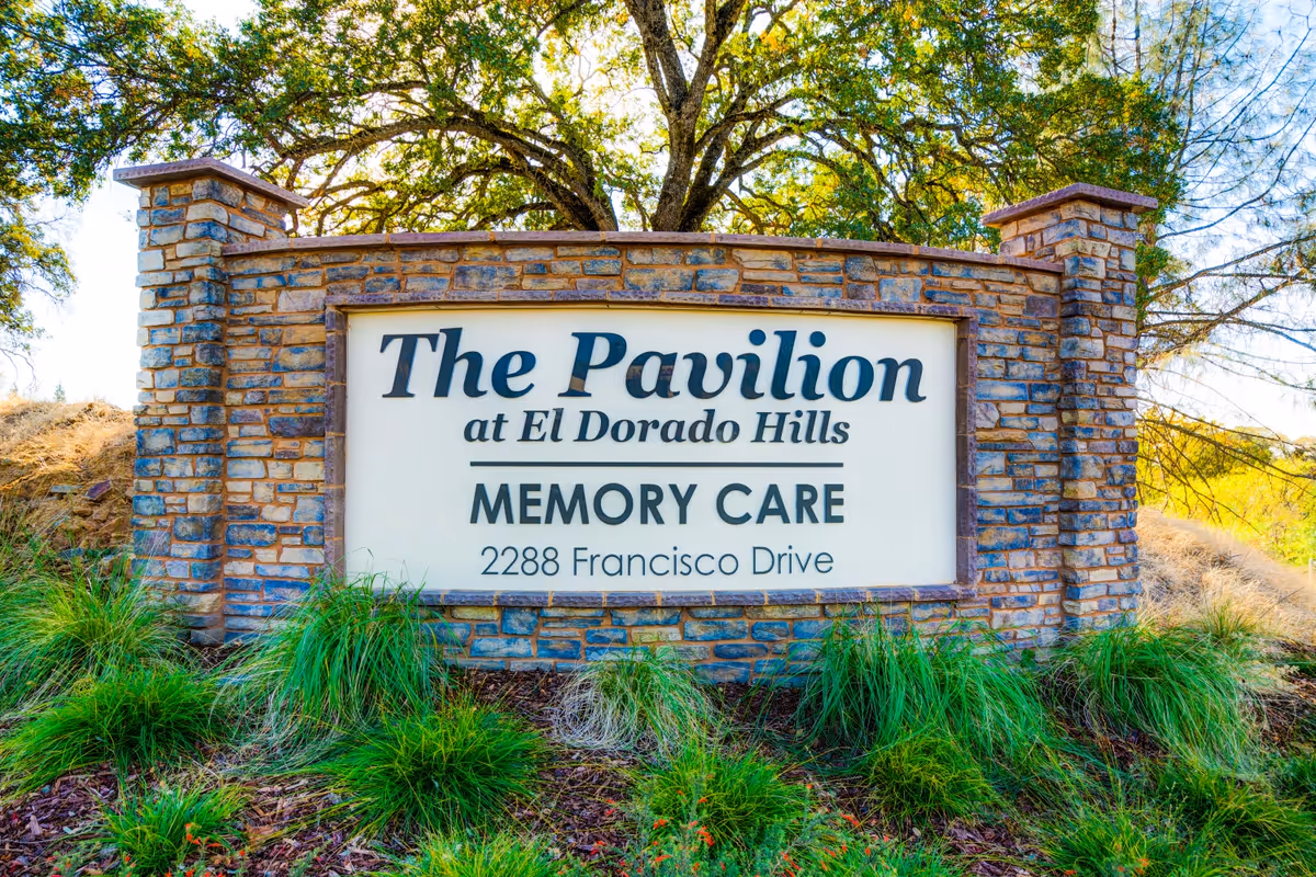Stone sign for The Pavilion at El Dorado Hills Memory Care located at 2288 Francisco Drive, surrounded by green grass and trees in the background.