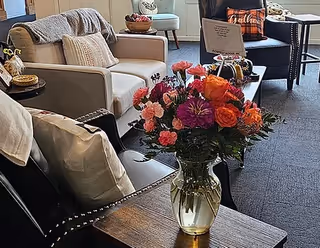 A cozy senior living lounge with sofas, cushions, and a vase of flowers.
