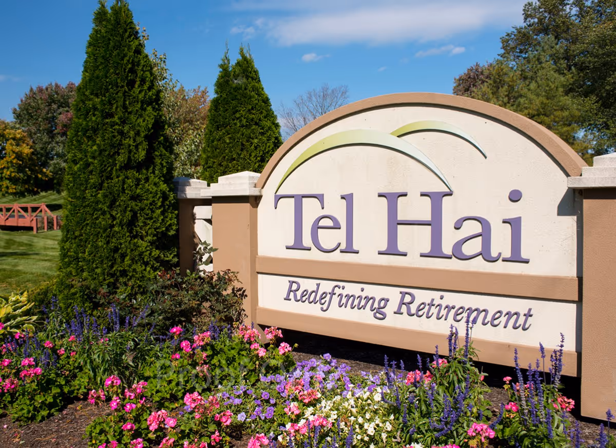 Outdoor entrance sign for Tel Hai Retirement Community surrounded by colorful flowers and greenery under a blue sky.
