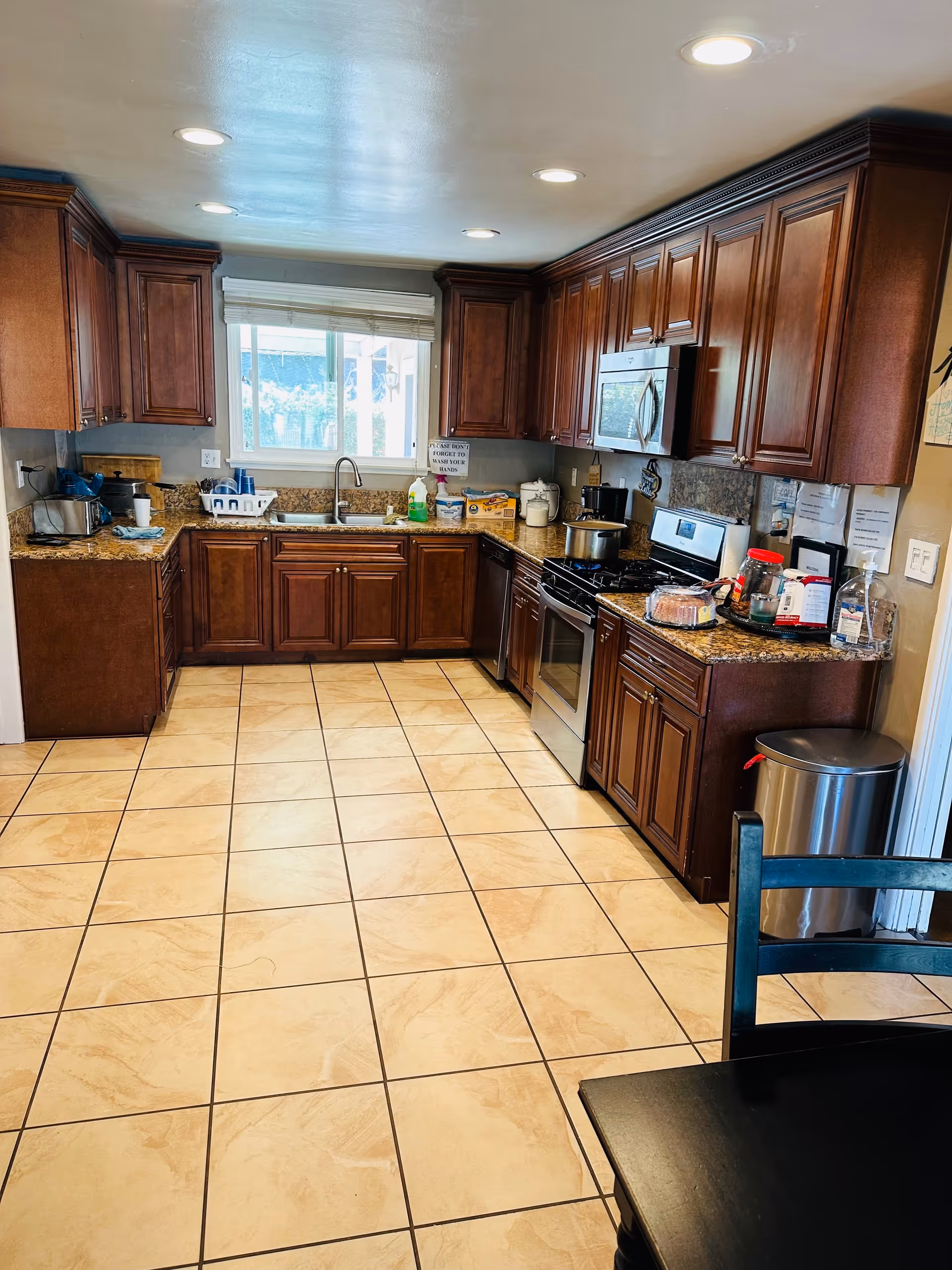 Bright kitchen with tiled floor, dark wood cabinets, granite countertops, stainless steel appliances, and a window above the sink.