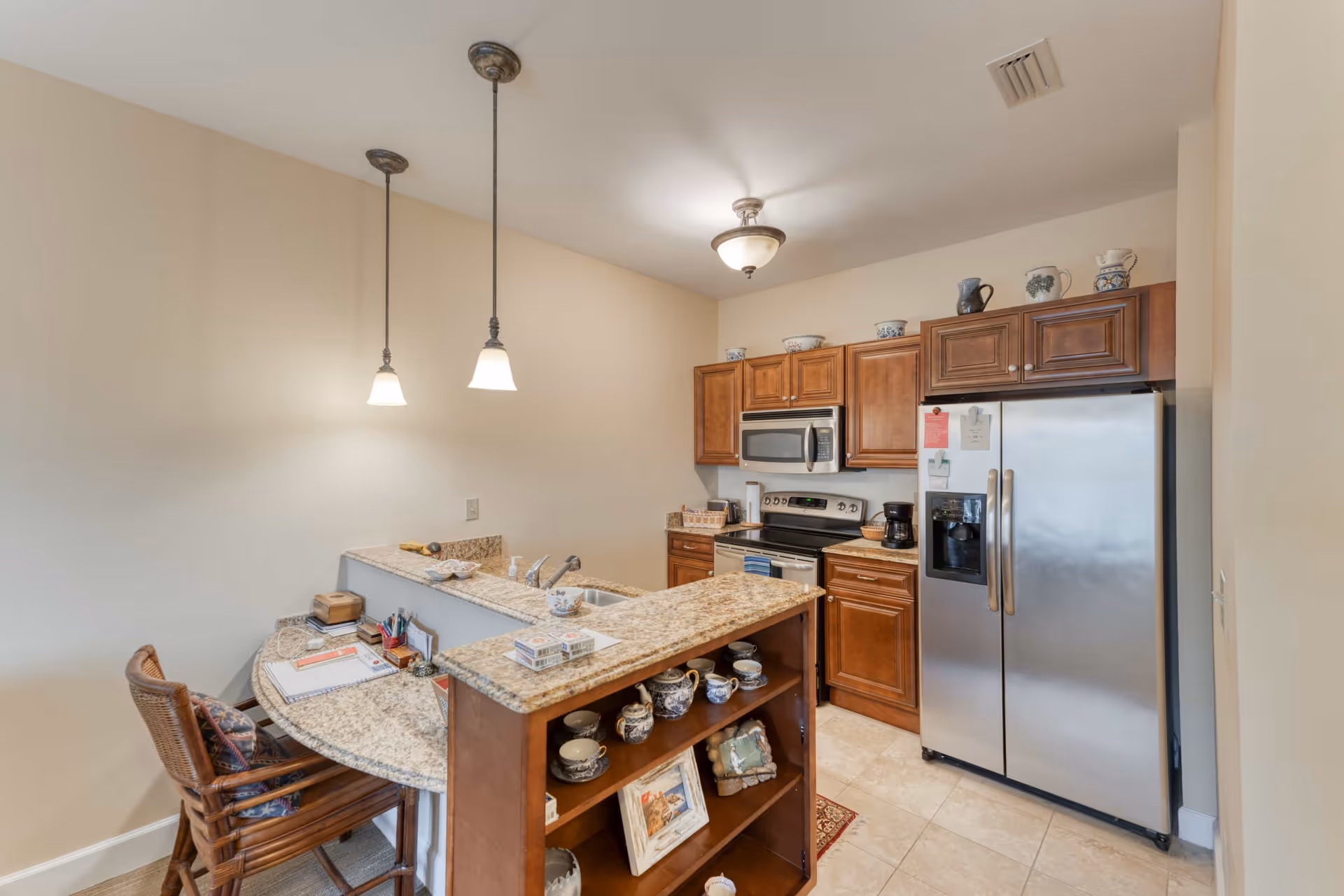 Kitchen with a granite island and bar seating, wooden cabinets, stainless-steel appliances, and pendant lighting.