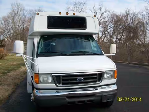 Front view of a white shuttle bus parked on a road with leafless trees behind.