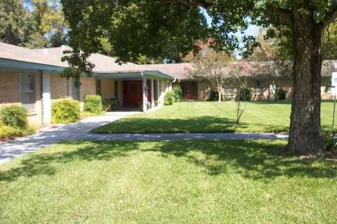 Exterior view of a single-story senior living facility with green lawn and trees.