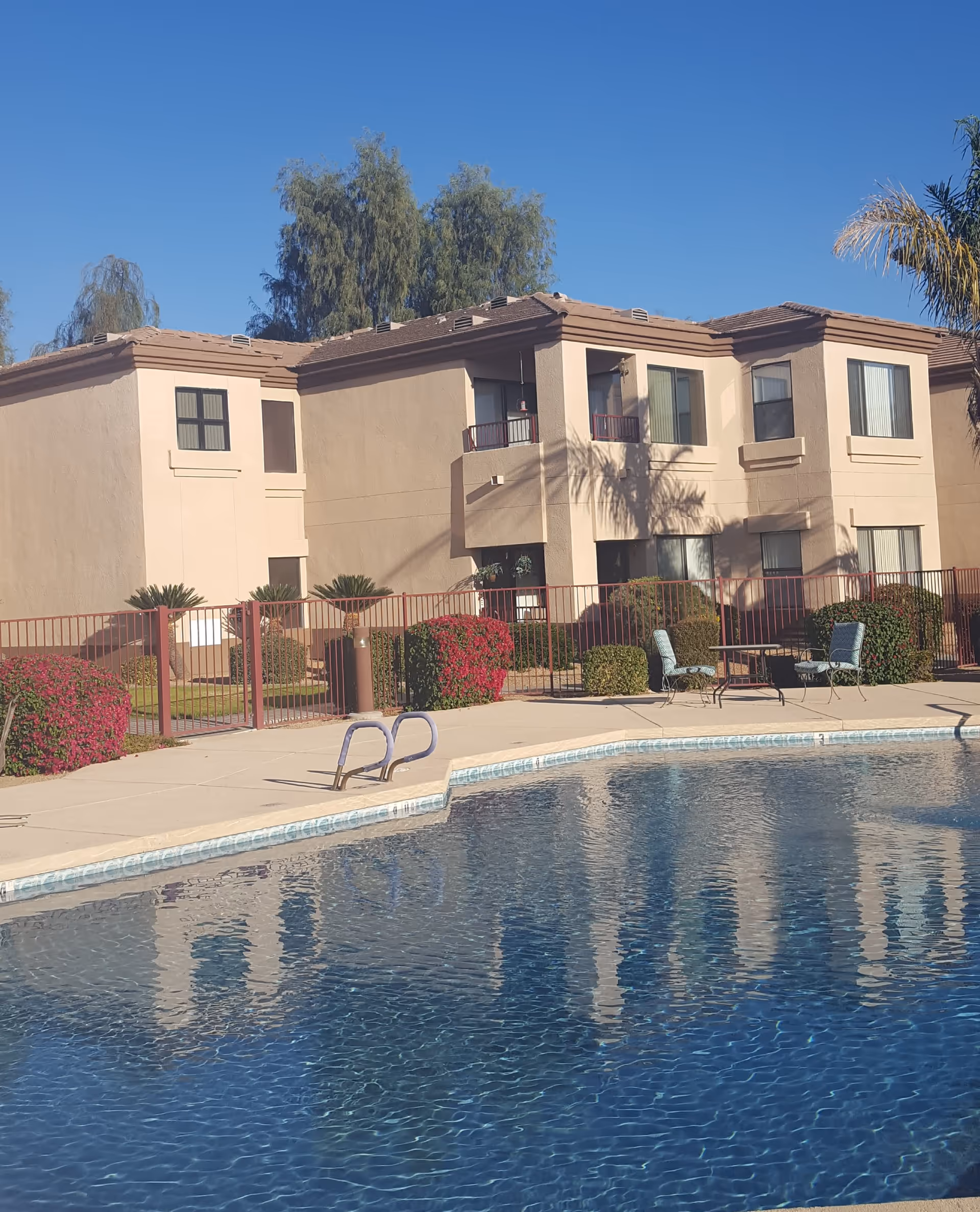 Outdoor view of a two-story beige apartment building with balconies and a swimming pool in the foreground.
