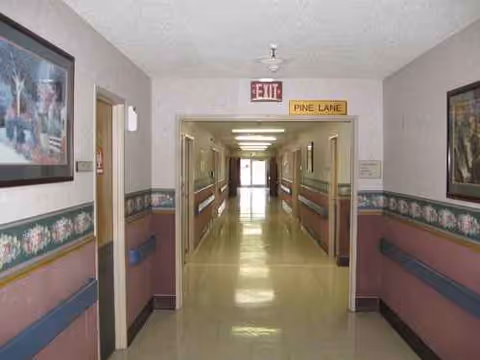 Interior hallway in a senior living facility with handrails and exit sign.