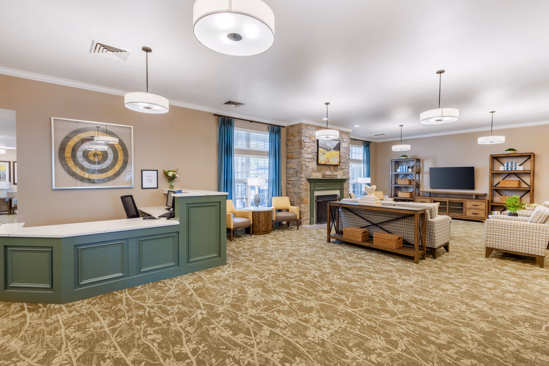 Bright senior living common lounge with a reception desk, seating area, stone fireplace, TV and bookshelves.