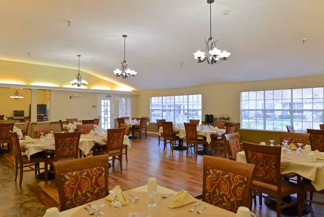 Spacious dining room with multiple set tables and patterned chairs, chandeliers, and large windows overlooking the outside.