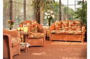 Sunlit sitting area with wicker sofa and chairs with patterned cushions, a small side table with drinks, and floor-to-ceiling windows with blinds.