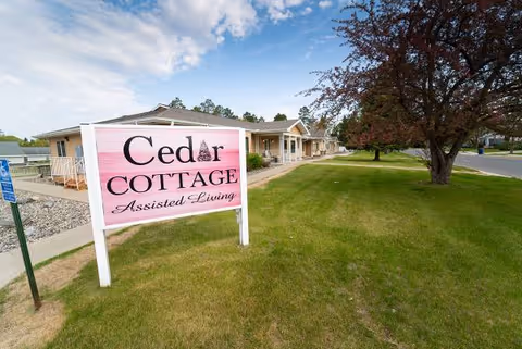 Front exterior of Cedar Cottage Assisted Living with pink sign on green lawn.