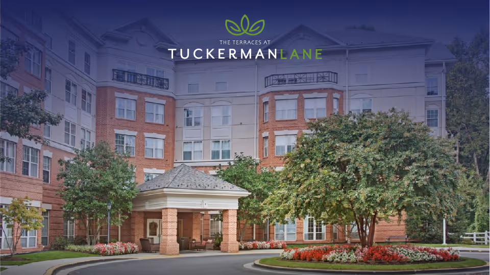 Front exterior of The Terraces at Tuckerman Lane showing the covered entrance/porte-cochère, landscaped roundabout, and the facility logo across the top.