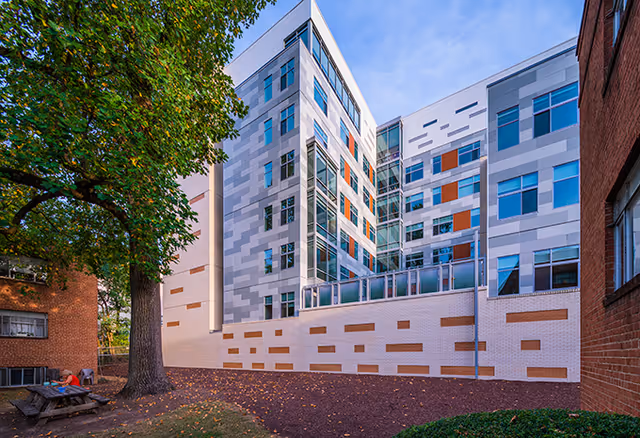 Exterior view of a modern multi-story residential building with a patterned façade and a large tree in the foreground.