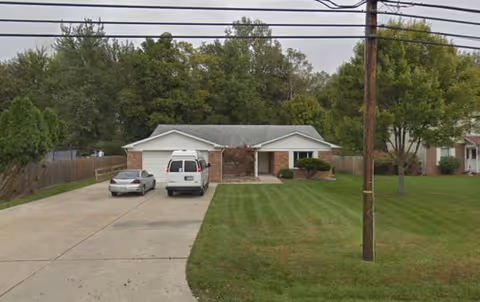 Front exterior of a single-story facility with driveway, lawn, and parked vehicles.