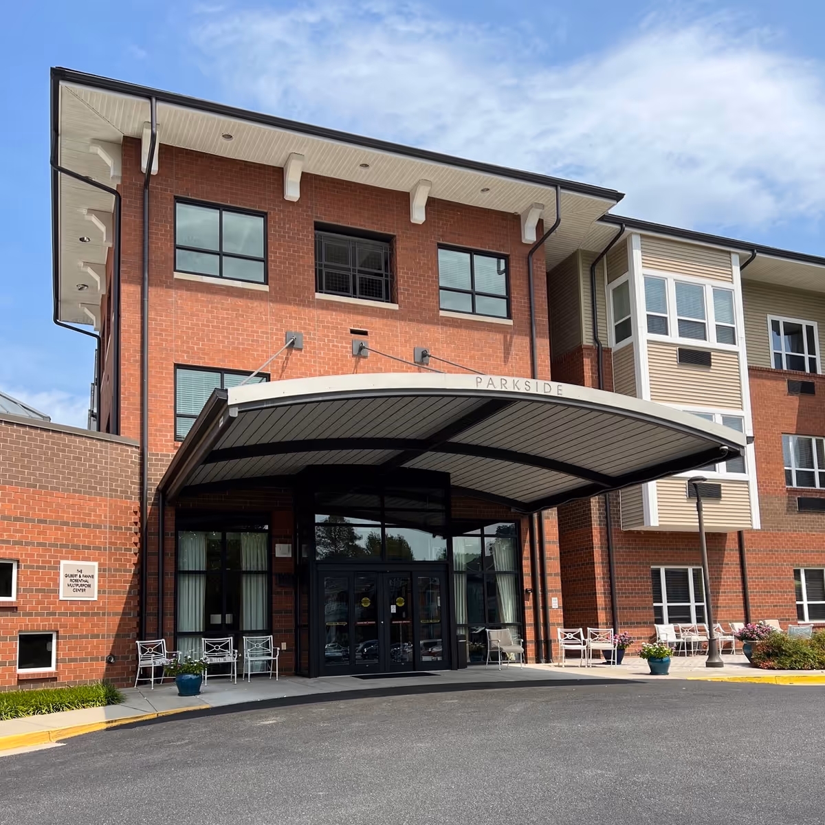 Brick senior living facility exterior with glass entry and curved metal canopy.
