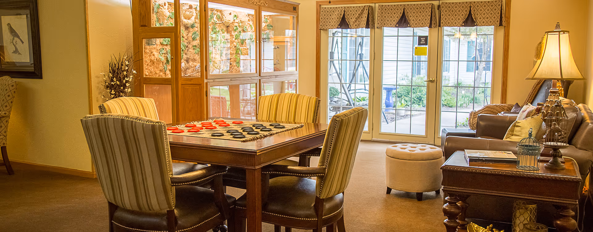 Cozy communal living room with a game table and chairs, sofas, lamps, and glass doors leading outside.