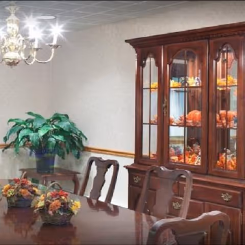 Formal dining room with a polished wooden table and chairs, chandelier, china cabinet displaying seasonal décor, and a potted plant.