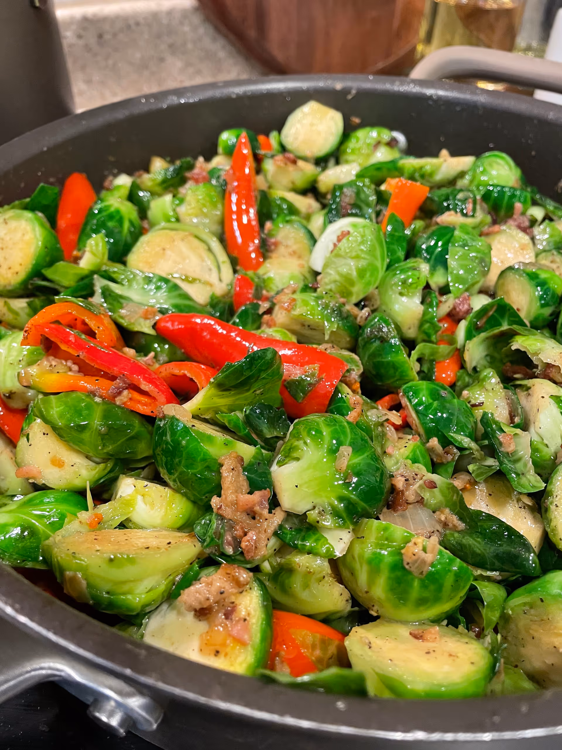 Close-up of a pan filled with cooked Brussels sprouts mixed with red bell peppers and bits of bacon or ground meat, seasoned and sautéed.