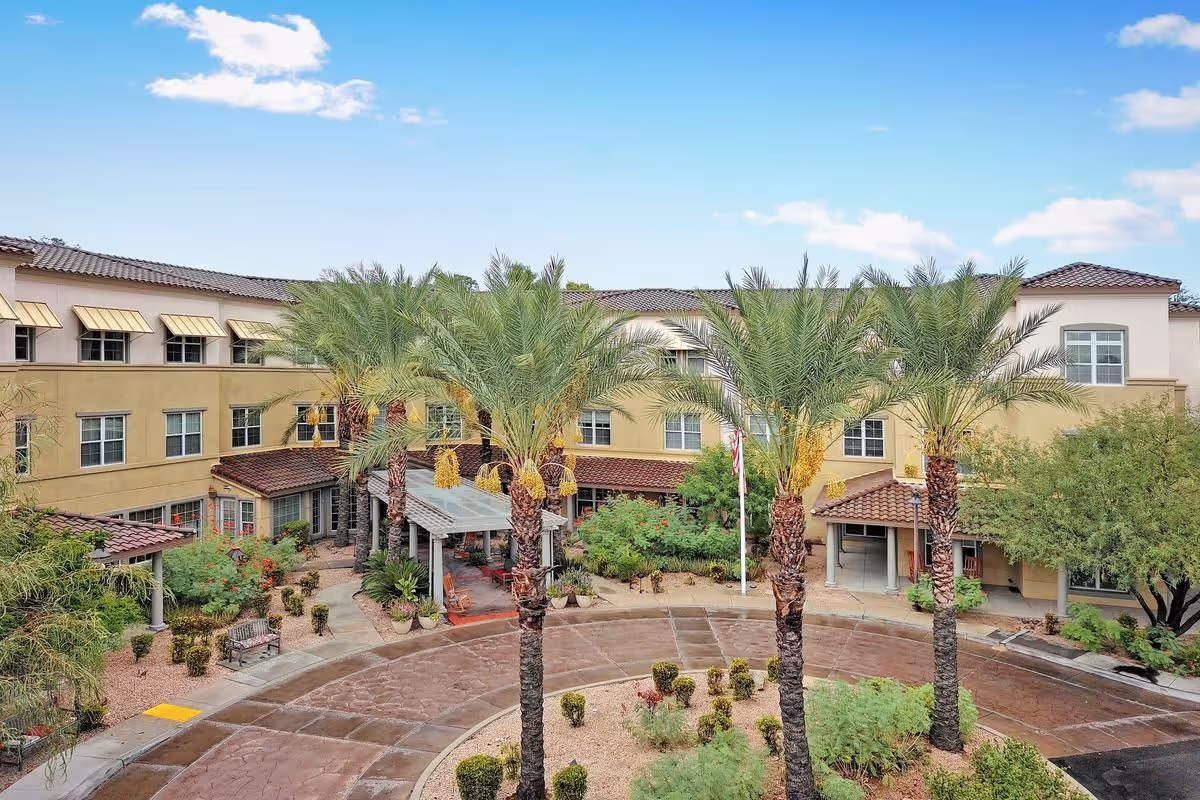 Exterior front of a three-story senior living facility with a circular driveway, palm trees, and a landscaped entrance courtyard.