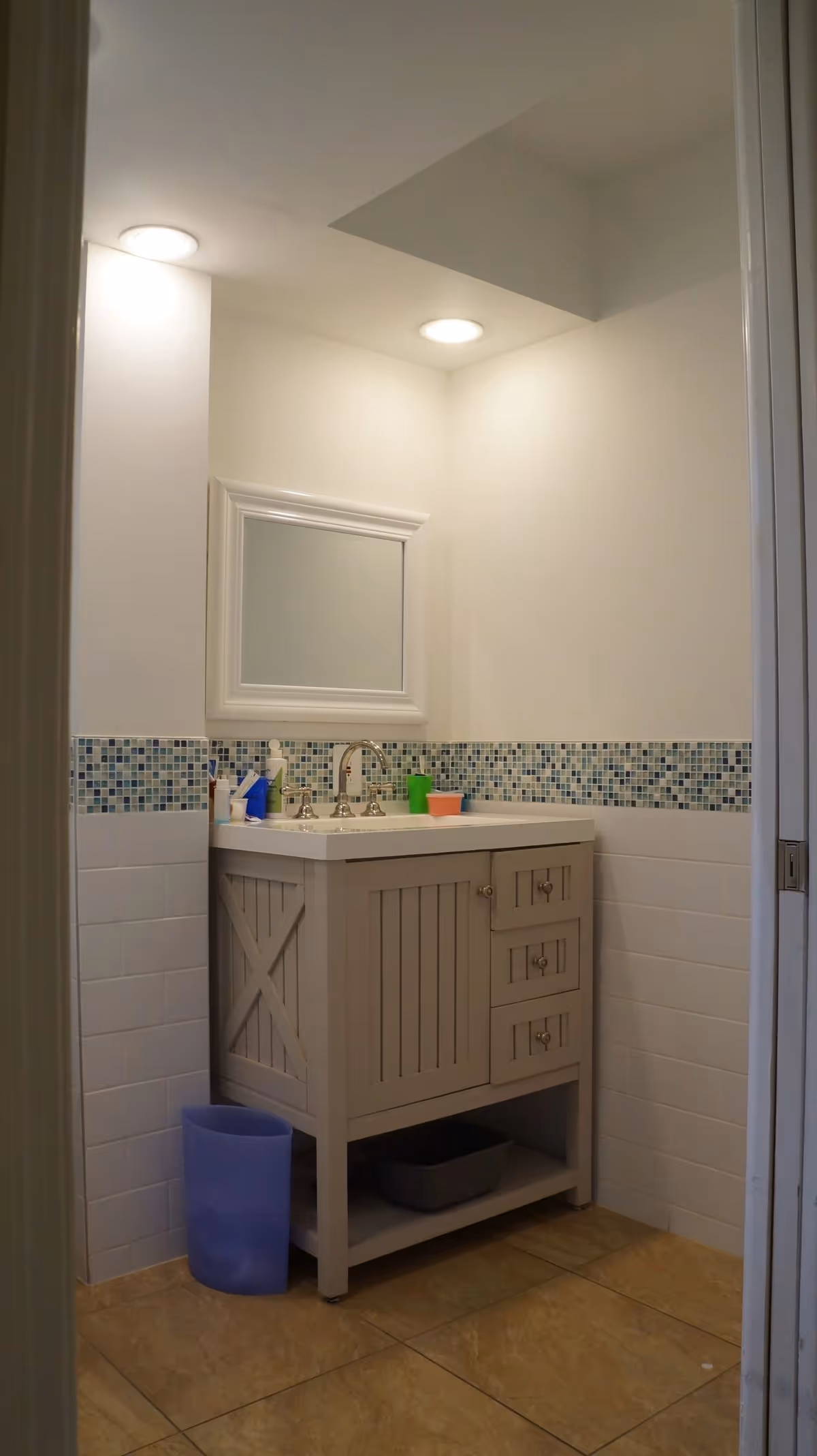 Bathroom vanity with sink and mirror, mosaic tile backsplash, recessed ceiling lights and a waste bin.