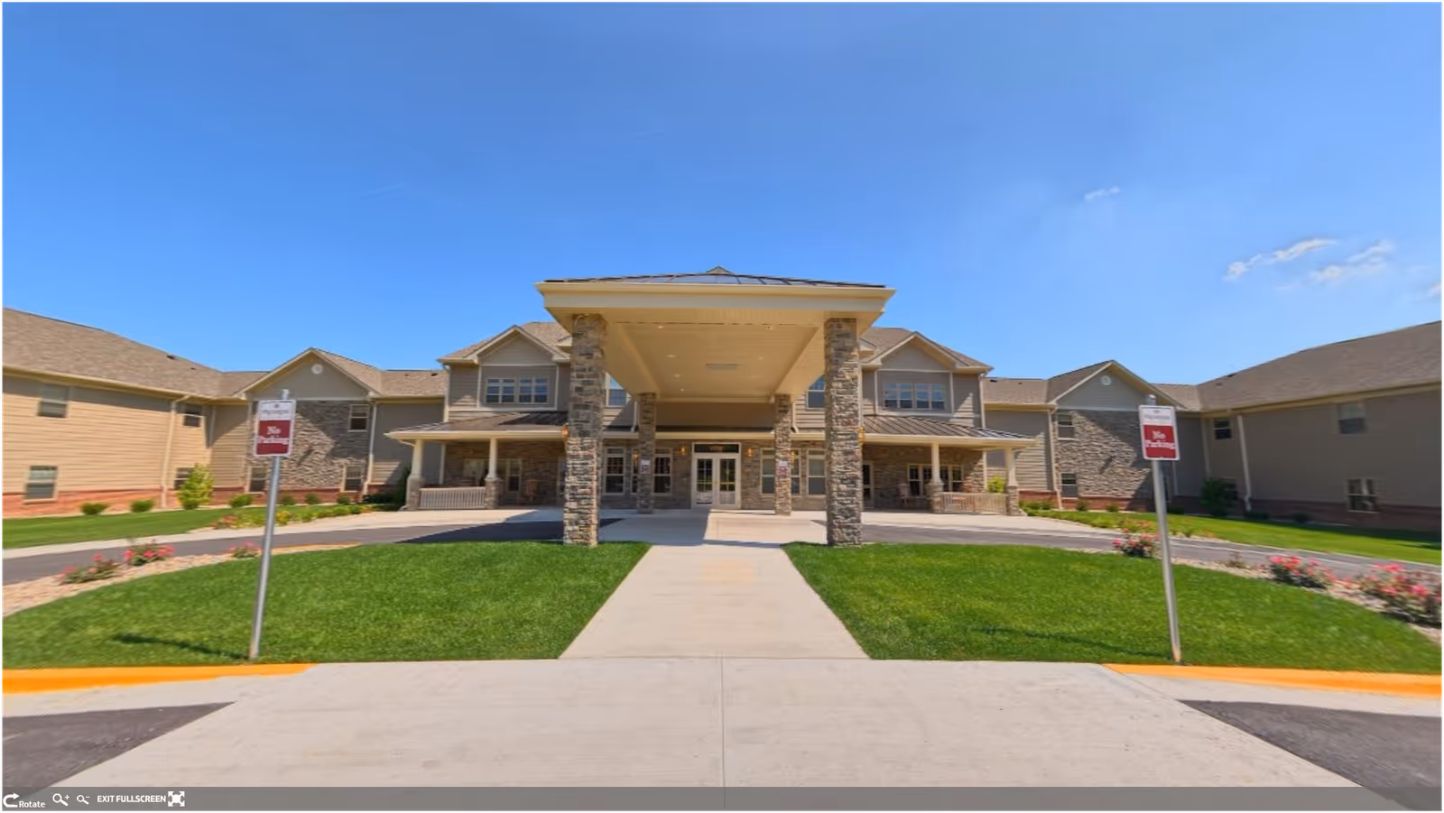 Front entrance of a retirement community building with a covered porte-cochère, stone columns, and landscaped lawn.