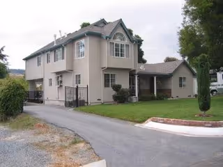 Two-story beige care home with driveway, front entrance, and well-kept lawn.