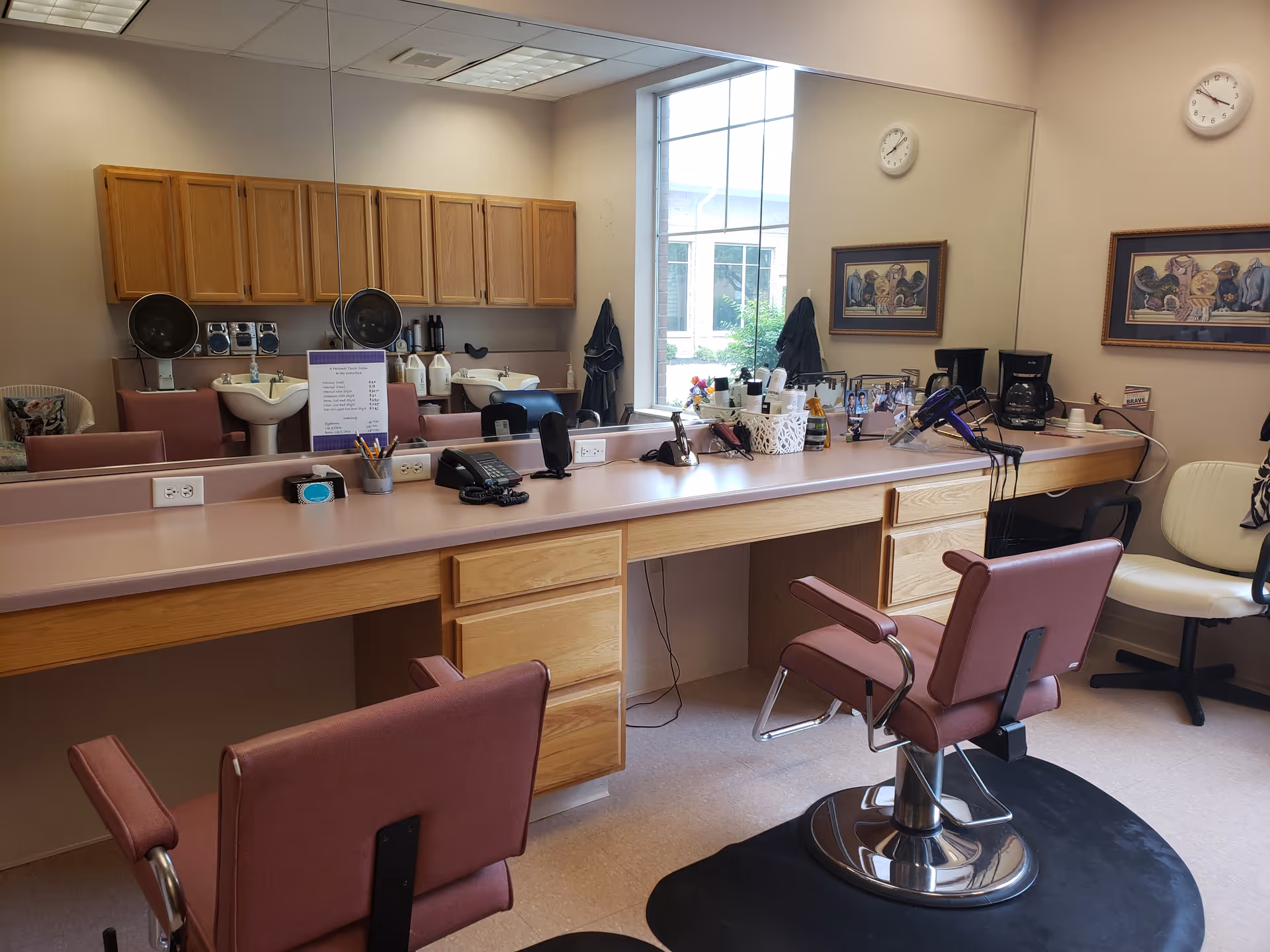 Hair salon station with styling chairs, large mirror, wash sinks and hair tools in a senior living facility.