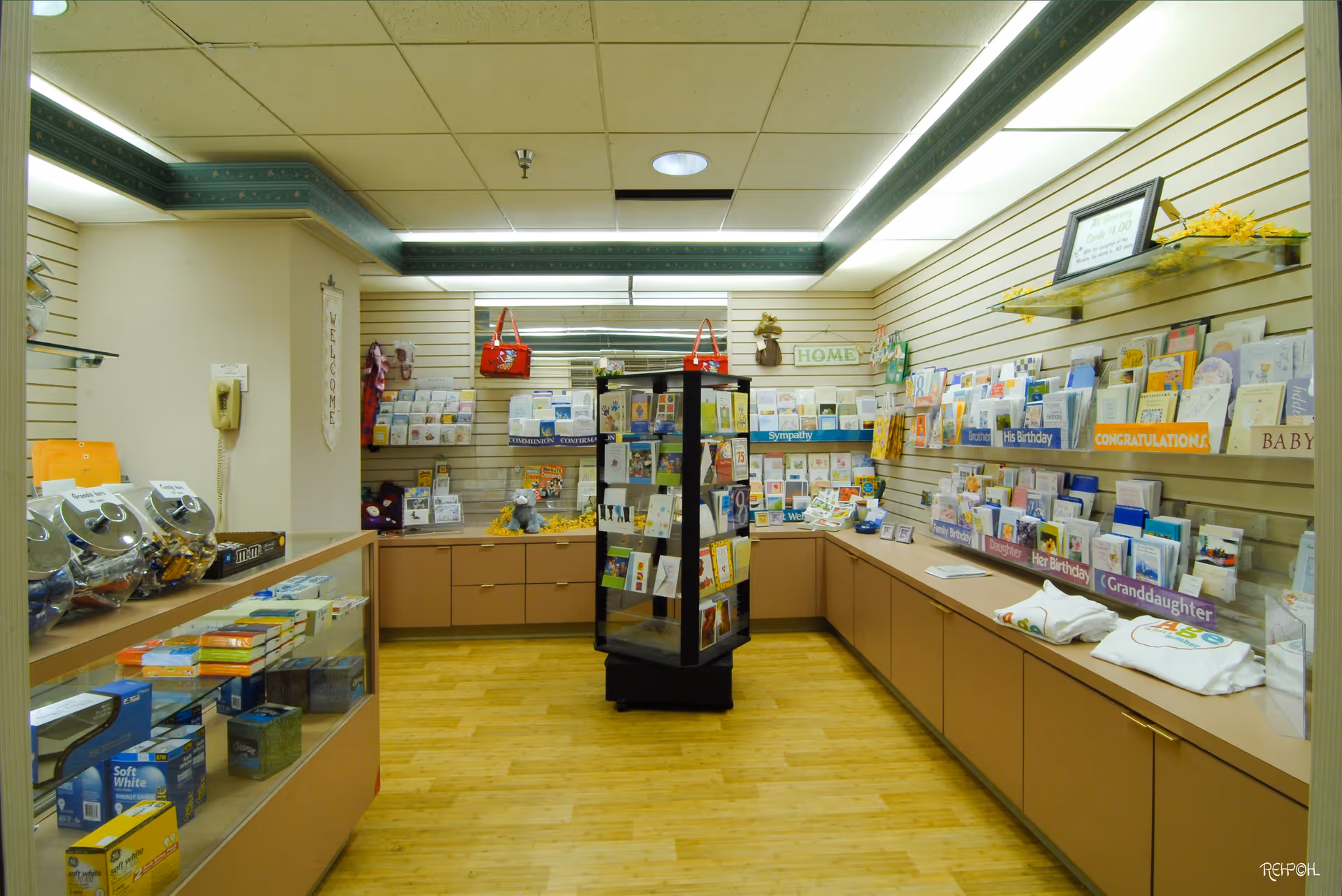 Small gift shop interior with greeting cards and merchandise displayed on shelves and a central rotating rack.