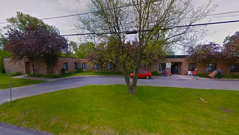 Exterior view of Evergreen Heights senior living building with green lawn and people near entrance.