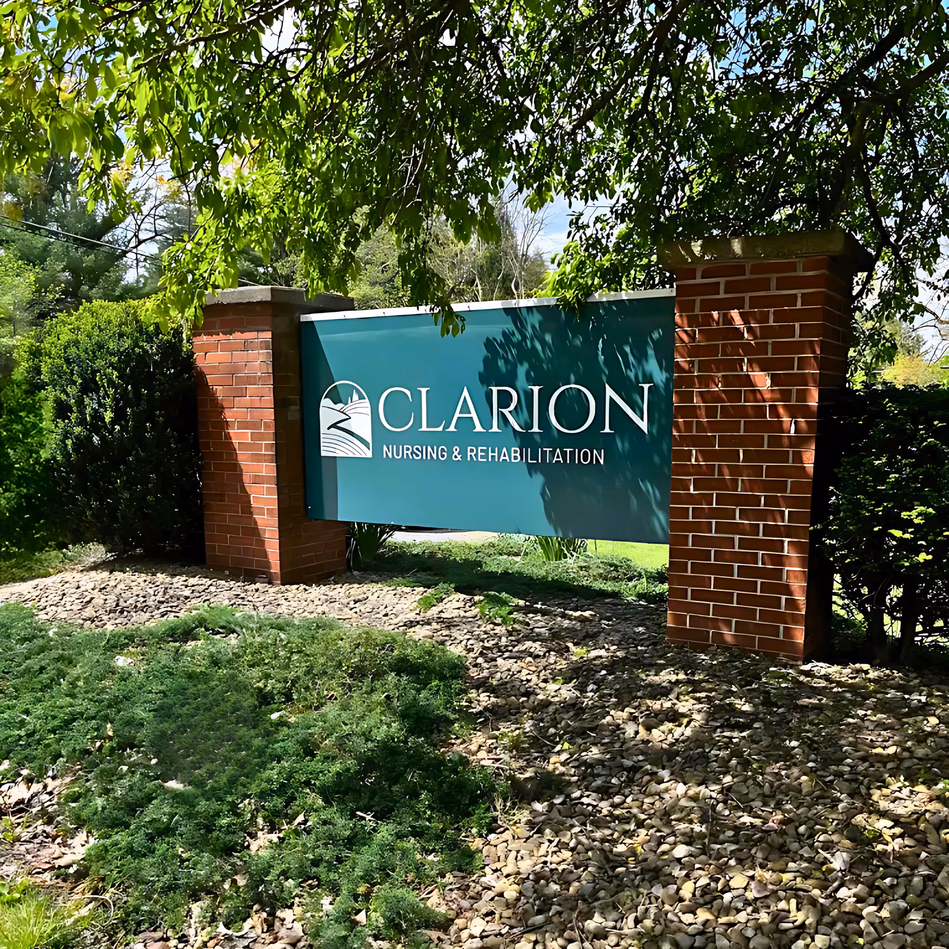 Outdoor sign for Clarion Nursing & Rehabilitation mounted between two brick pillars with greenery and trees surrounding it.