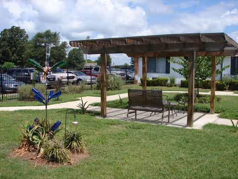 Outdoor seating area under a wooden pergola in a grassy courtyard at a senior facility.
