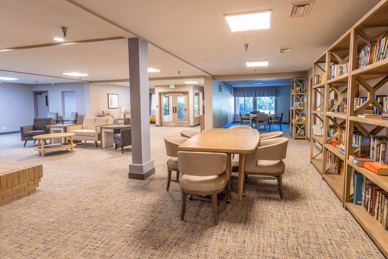 Spacious senior living common area with tables, chairs, sofas and bookshelves.