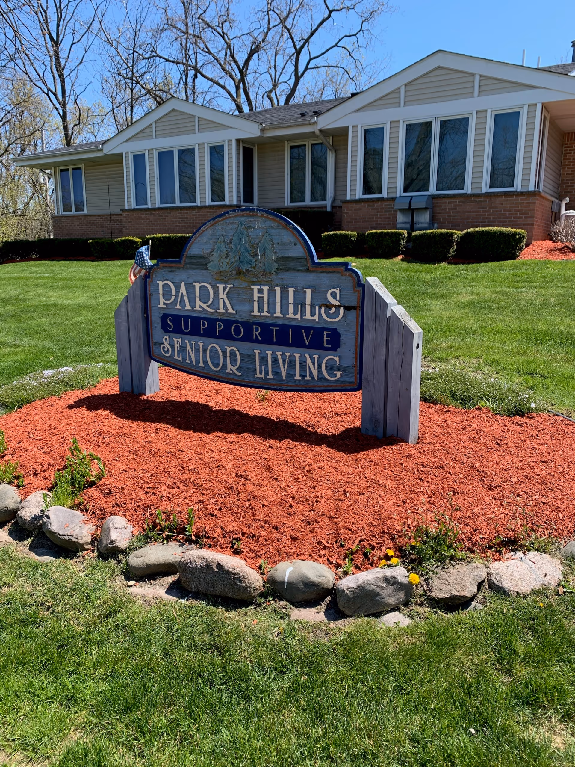 A wooden sign reading "Park Hills Supportive Senior Living" sits on red mulch in front of a single-story assisted living building.