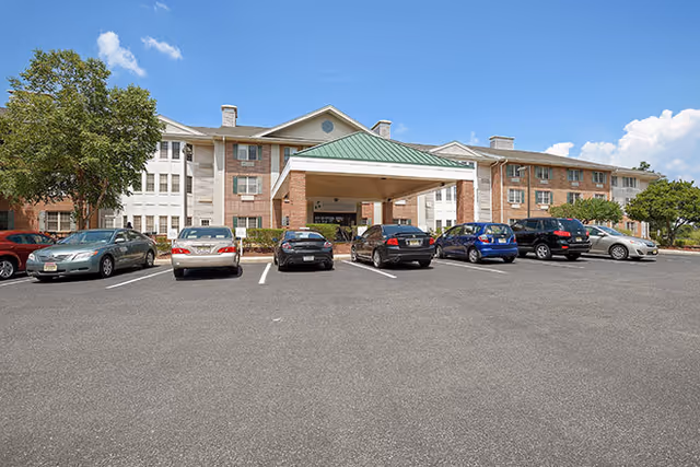 Front exterior view of Brookdale Monroe senior living facility with a covered entrance and several parked cars in the parking lot under a clear blue sky.
