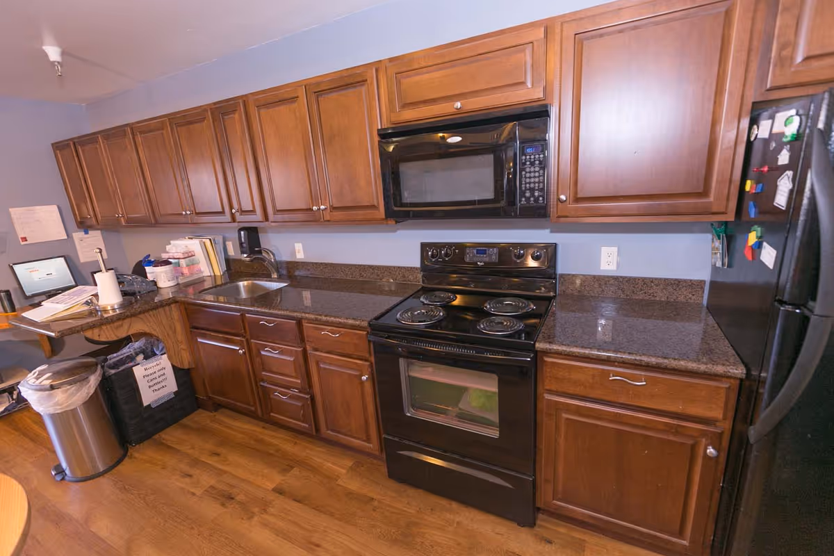 Kitchenette with dark wood cabinets, granite countertops, a sink, electric stove with microwave above, and a refrigerator.