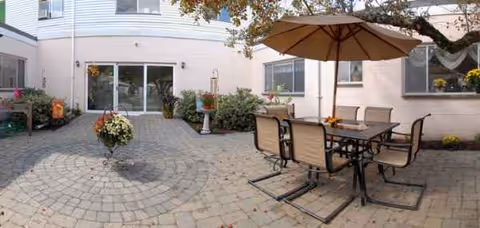 Courtyard patio with outdoor table, umbrella, and potted plants beside a light-colored building.
