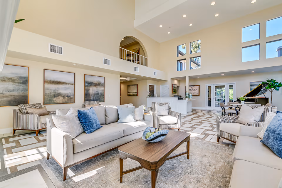 Bright, airy communal living room with sofas, armchairs, a coffee table, high ceilings and a grand piano.