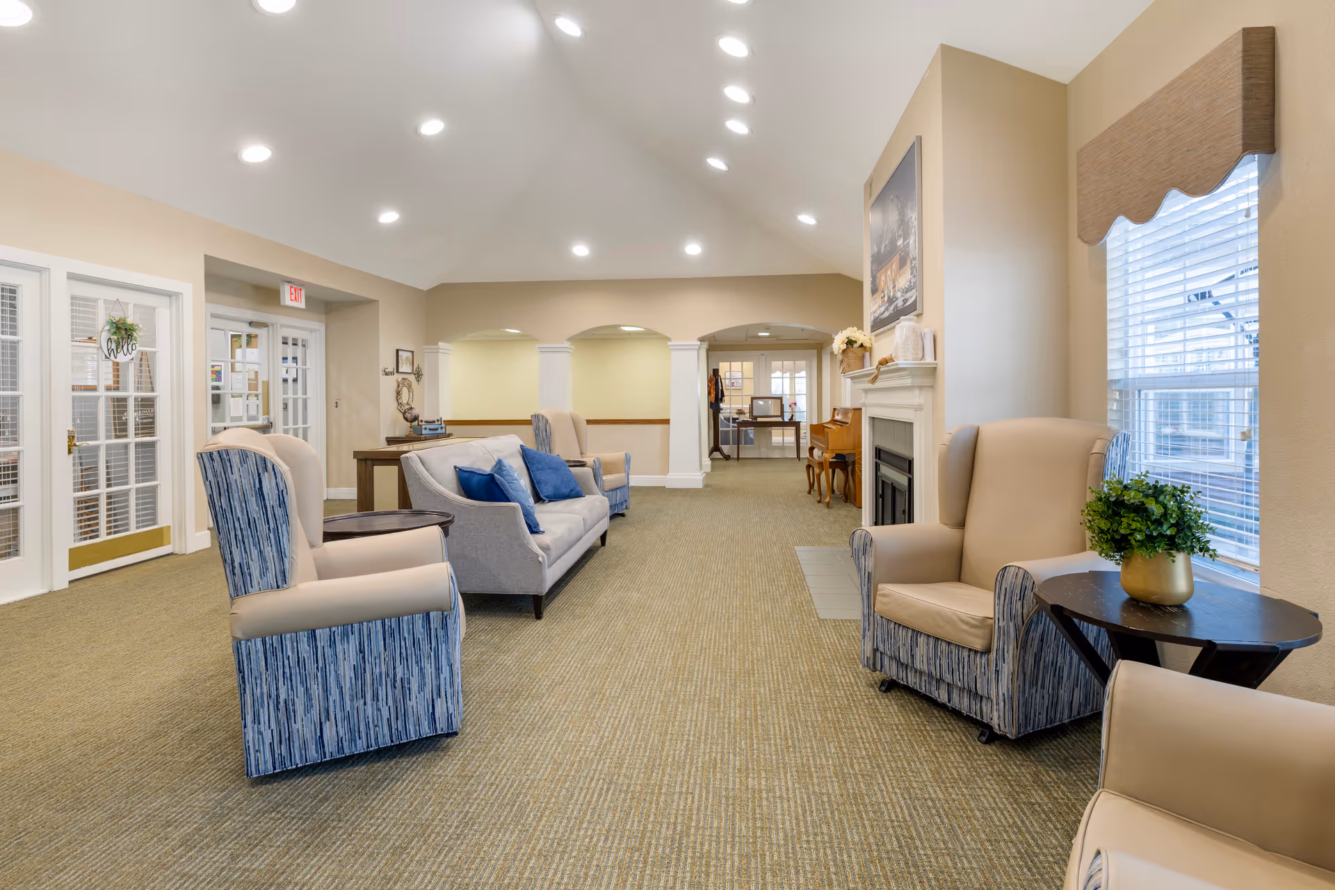 Bright, spacious senior living lounge with armchairs, sofas, a fireplace, and large windows.