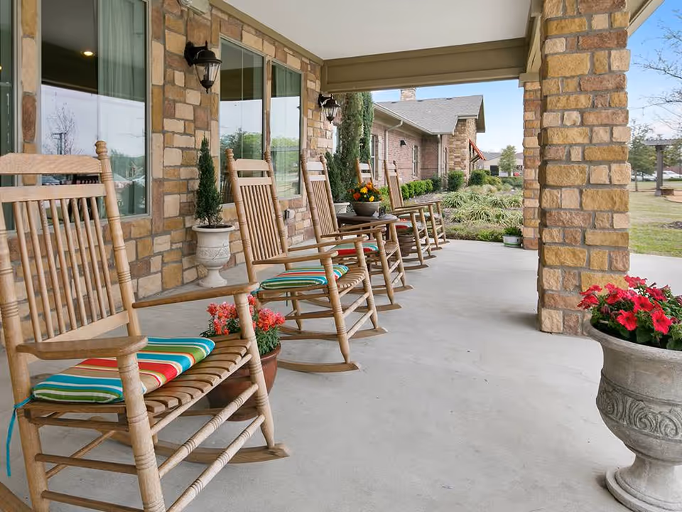 Covered stone-front porch with a row of wooden rocking chairs and potted flowers.